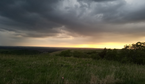 A dramatic sky with dark clouds and a golden sunset over a green landscape, creating a serene and moody atmosphere.