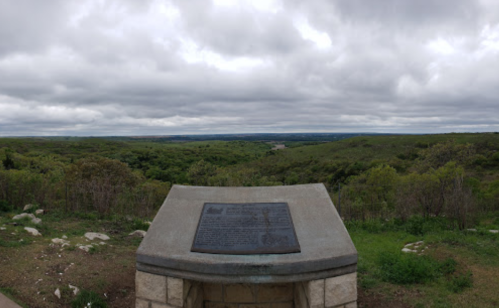 A stone monument with a plaque overlooks a lush green landscape under a cloudy sky.