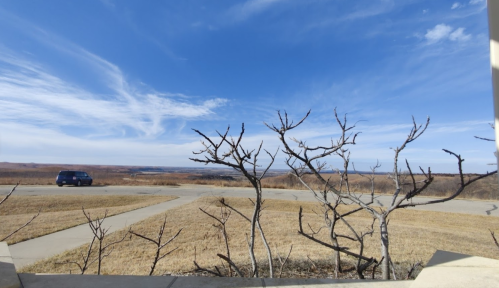 A barren landscape with a blue sky, a few scattered clouds, and a car driving on a winding road in the distance.