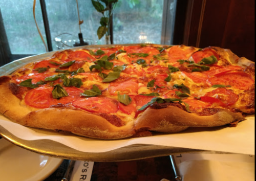 A freshly baked pizza topped with tomatoes and basil, served on a metal tray.