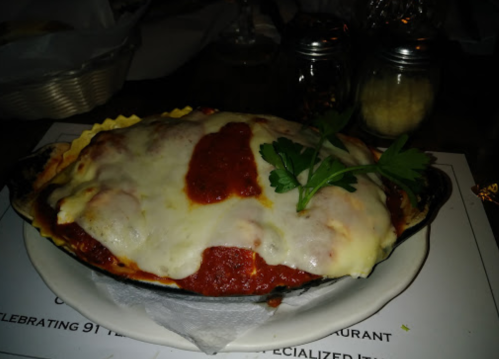 A baked lasagna dish topped with melted cheese and marinara sauce, garnished with a sprig of parsley.
