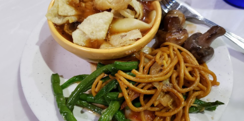 A plate of food featuring noodles, green beans, mushrooms, and a bowl of crispy snacks in sauce.