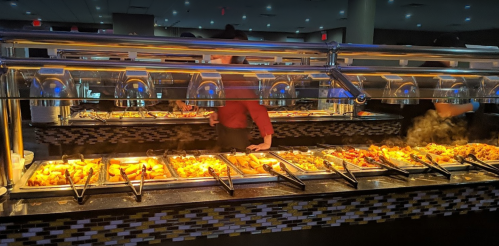 A buffet with various dishes displayed under warming lights, with a server in the background.