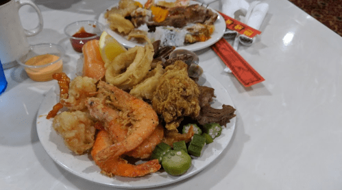 A plate of assorted fried seafood, chicken, and vegetables, with dipping sauces and a lemon wedge on a table.