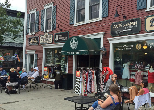 A quaint street scene featuring shops, outdoor seating, and people dining in a charming town.