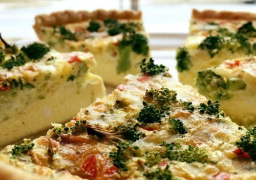 A close-up of a sliced vegetable quiche with broccoli and tomatoes, arranged on a plate.