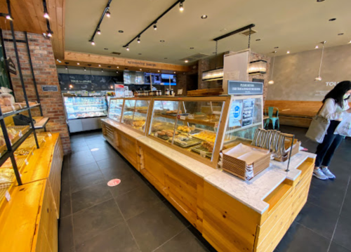 A bakery display with various pastries and bread, featuring a wooden counter and a customer browsing.