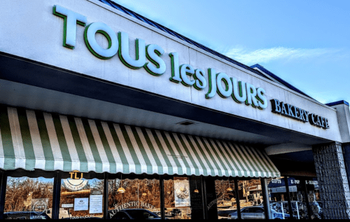 Exterior of Tous les Jours Bakery Café, featuring a green sign and striped awning.