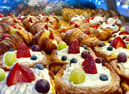 A display of pastries featuring croissants and cream-filled treats topped with strawberries, blueberries, and grapes.