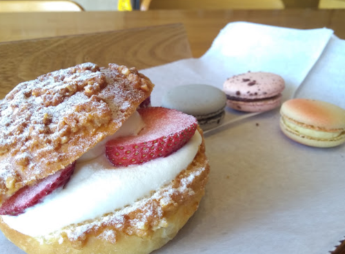 A dessert featuring a strawberry-topped pastry with cream, alongside three colorful macarons on a paper tray.