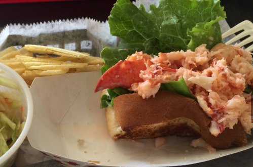 A lobster roll topped with fresh lobster meat and lettuce, served with a side of fries and coleslaw.