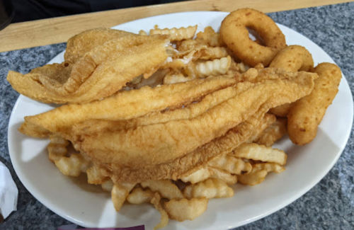 A plate of golden fried fish fillets, crinkle-cut fries, and onion rings.