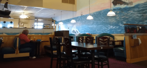 A cozy restaurant interior with nautical-themed decor, featuring booths, tables, and a mural of a ship and ocean.