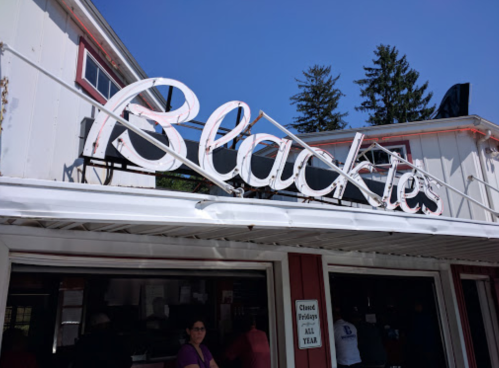 Sign for "Blackie's" restaurant with a clear blue sky and trees in the background. People are visible near the entrance.