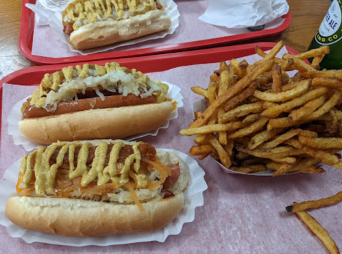 Two hot dogs topped with mustard and sauerkraut, served with a side of crispy French fries on a red tray.