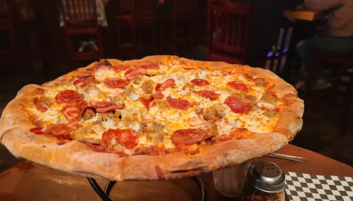 A large pizza topped with pepperoni and sausage, served on a wooden table in a restaurant setting.
