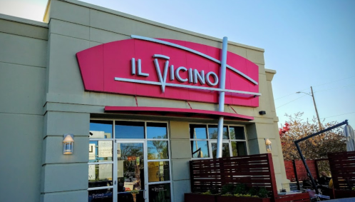 Exterior of a restaurant named "Il Vicino," featuring a bright pink sign and large windows.