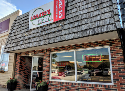 Exterior of Lomato's Pizza with a shingled roof, "OPEN" neon sign, and brick facade. A person is entering the restaurant.