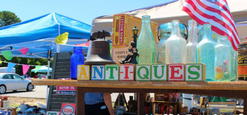 A colorful display of vintage bottles and a sign reading "ANTHQUES" at an outdoor market with tents and flags.