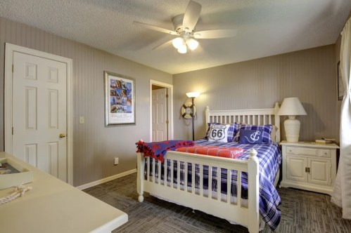 Cozy bedroom with a white bed, blue plaid bedding, a ceiling fan, and light-colored walls.