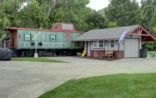 A vintage green train car next to a small red-roofed building in a grassy area.