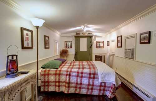 Cozy bedroom with a plaid quilt, lamp, and framed pictures, featuring a green door and air conditioning unit.