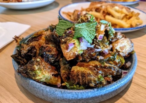 A bowl of crispy Brussels sprouts garnished with mint and diced onions, served on a wooden table.