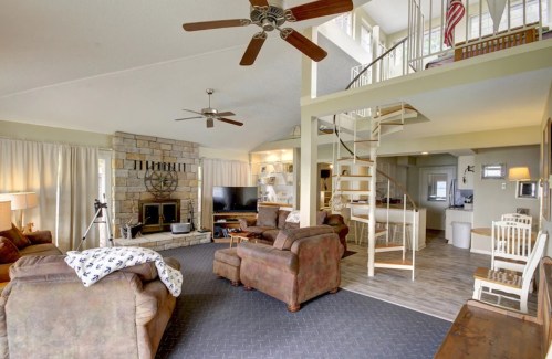 Spacious living room with stone fireplace, comfortable seating, and a spiral staircase leading to an upper level.