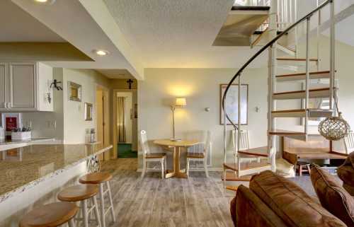 Cozy interior featuring a spiral staircase, dining area, and a kitchen bar with stools in a well-lit space.