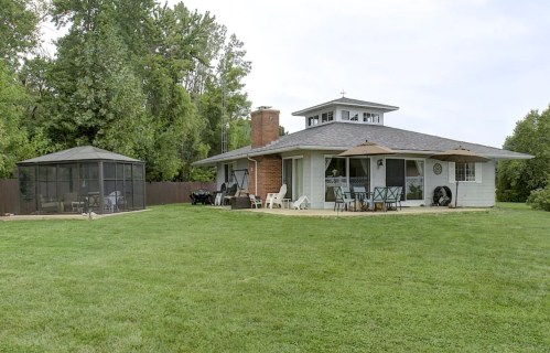 A spacious backyard featuring a house, a gazebo, and green grass under a cloudy sky.