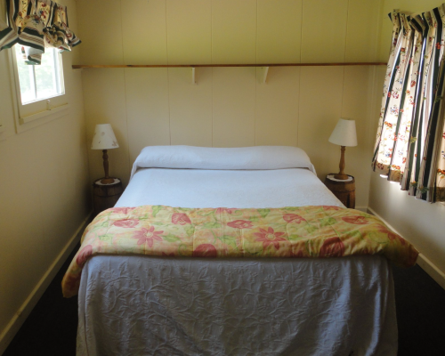 A cozy bedroom featuring a double bed with a floral blanket, two bedside lamps, and patterned curtains.