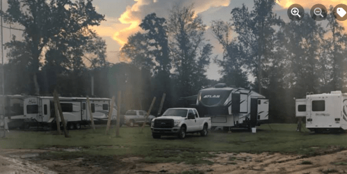 A campsite with several RVs and a white truck under a cloudy sky at sunset.