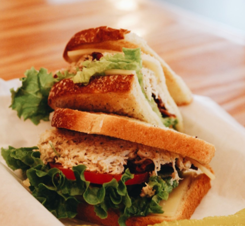 A sandwich with layers of lettuce, tomato, and chicken salad, served on toasted bread with a pickle on the side.