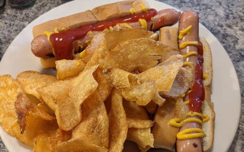A plate with two hot dogs topped with ketchup and mustard, served alongside a pile of crispy potato chips.
