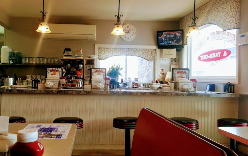 A cozy diner interior featuring a counter with stools, condiments on tables, and a TV in the background.