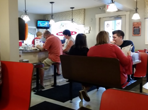 A cozy diner scene with patrons seated at a counter and tables, enjoying meals and chatting in a casual atmosphere.
