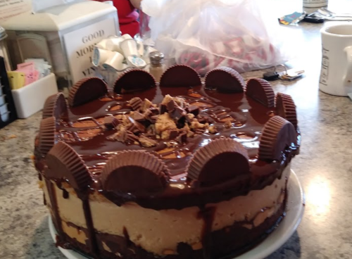 A chocolate cake topped with peanut butter cups and chocolate drizzle, sitting on a countertop.