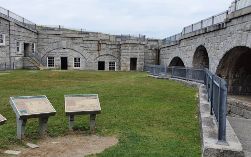 Historic stone fort interior with grassy courtyard and informational signs. Overcast sky in the background.