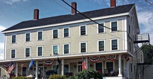 Historic building with a light-colored facade, multiple windows, and American flags, featuring a staircase on the side.