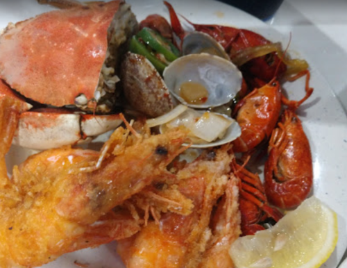A plate of seafood featuring fried shrimp, crab, crawfish, clams, and lemon wedges.
