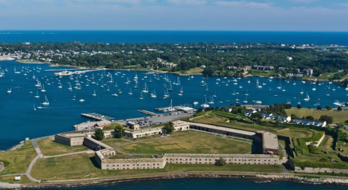Aerial view of a coastal fort surrounded by water, boats, and greenery under a clear blue sky.