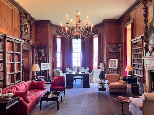 A cozy library with wooden walls, bookshelves, elegant furniture, and a chandelier, creating a warm, inviting atmosphere.