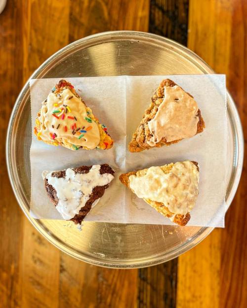 A silver platter with four assorted scones, each topped with different icing and colorful sprinkles.