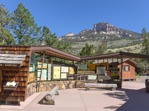 Visitor center with informational displays, surrounded by trees and mountains under a clear blue sky.