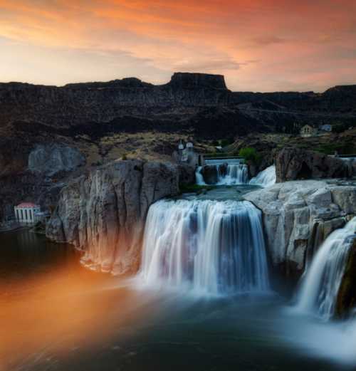 A stunning waterfall cascades over rocky cliffs at sunset, surrounded by lush greenery and dramatic skies.