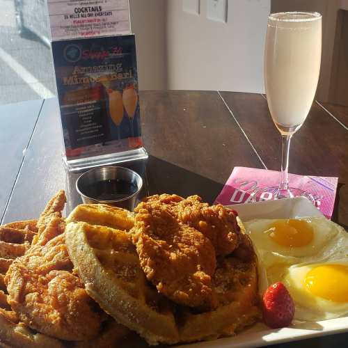 A plate of chicken and waffles with two sunny-side-up eggs, a strawberry, and a mimosa on the side.