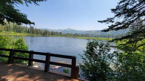 A serene lake surrounded by lush greenery and mountains under a clear blue sky.