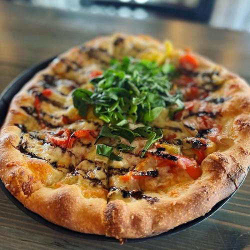 A freshly baked pizza topped with fresh greens, tomatoes, and drizzled with balsamic glaze on a wooden table.