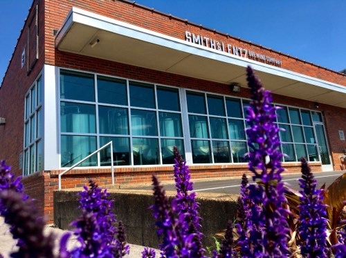Exterior of Smith & Fentz Brewing Company, featuring large windows and purple flowers in the foreground.