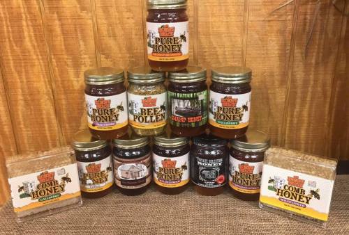 A display of various jars of honey, bee pollen, and comb honey arranged in a pyramid shape on a wooden background.